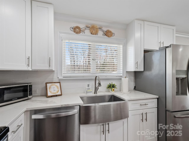 kitchen with light stone counters, decorative backsplash, appliances with stainless steel finishes, white cabinets, and a sink