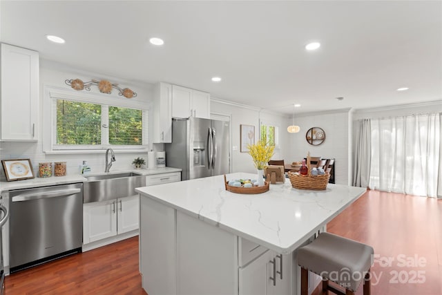 kitchen with stainless steel appliances, a kitchen island, a sink, and white cabinetry