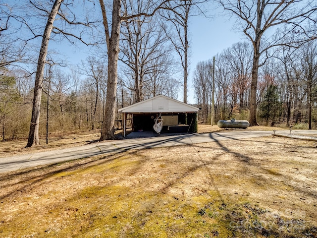 view of property exterior featuring dirt driveway, a view of trees, and a carport