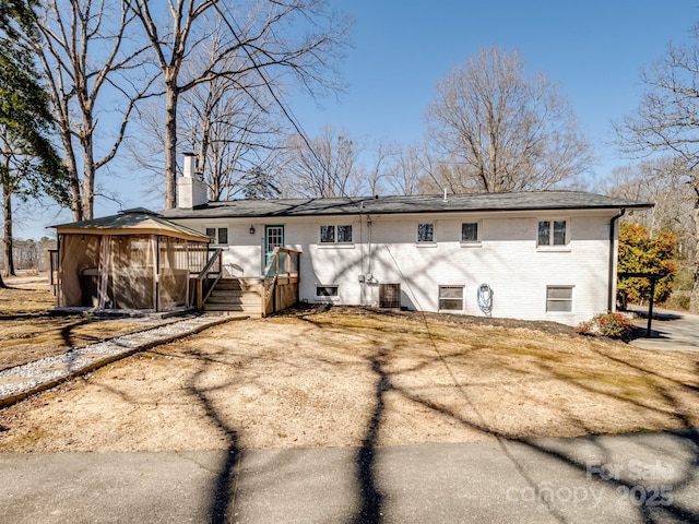 rear view of house featuring a deck, brick siding, a chimney, and central AC unit