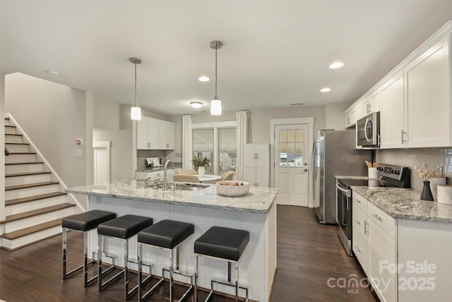 kitchen with appliances with stainless steel finishes, sink, white cabinets, hanging light fixtures, and a kitchen island with sink