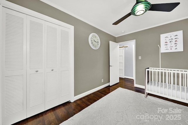 bedroom featuring dark hardwood / wood-style flooring, ceiling fan, a crib, crown molding, and a closet