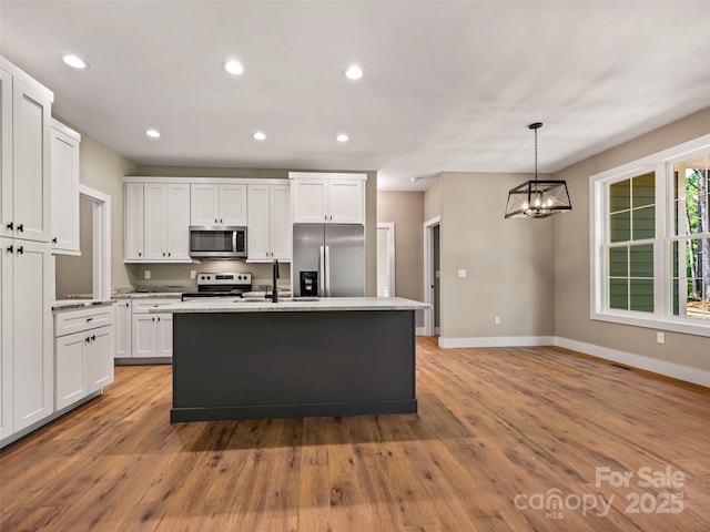 kitchen with appliances with stainless steel finishes, a center island, light hardwood / wood-style floors, white cabinets, and decorative light fixtures