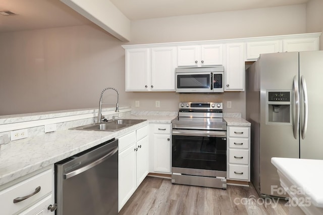 kitchen with appliances with stainless steel finishes, light wood-type flooring, light stone counters, sink, and white cabinetry