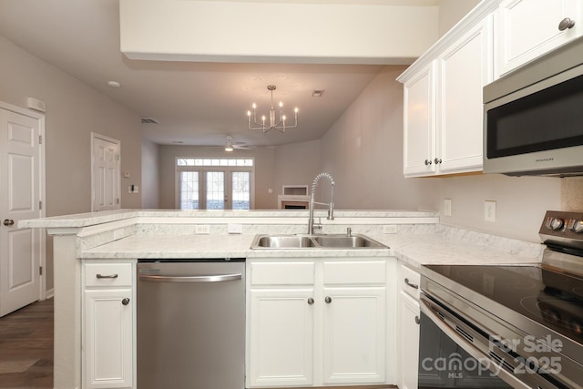 kitchen featuring appliances with stainless steel finishes, light stone counters, sink, white cabinetry, and kitchen peninsula