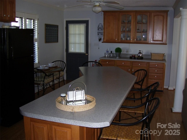 kitchen with ornate columns, hardwood / wood-style floors, ornamental molding, ceiling fan, and black fridge