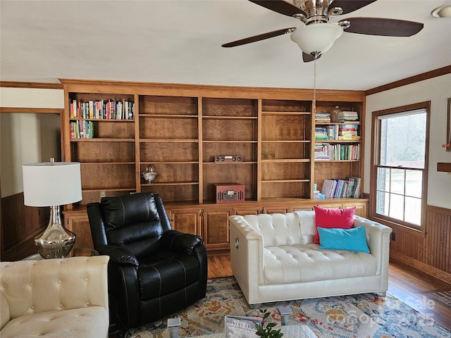 living area with hardwood / wood-style flooring, ornamental molding, ceiling fan, and wooden walls