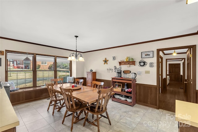 dining area featuring an inviting chandelier, ornamental molding, wooden walls, and light tile patterned floors