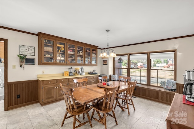 dining room featuring an inviting chandelier, light tile patterned floors, wooden walls, and ornamental molding