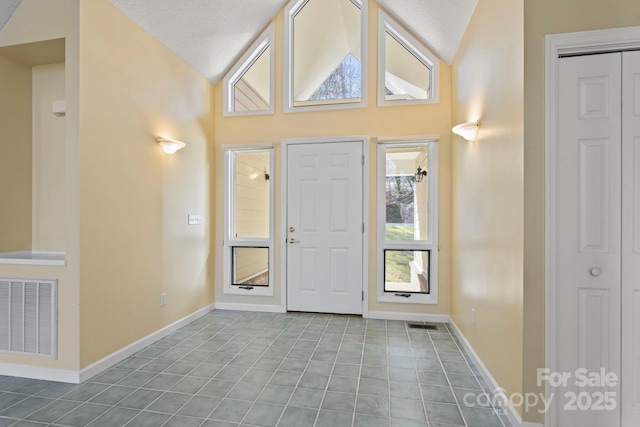 entryway with a textured ceiling, lofted ceiling, and light tile patterned flooring