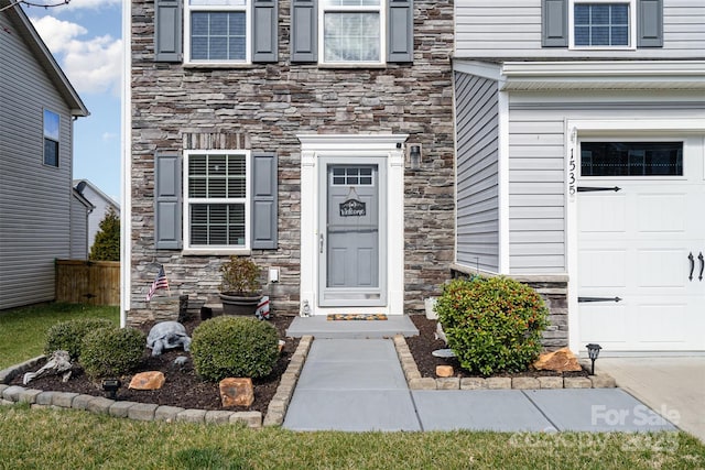 view of exterior entry featuring a garage, stone siding, and fence