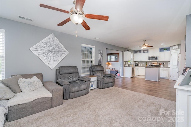 living room with recessed lighting, wood finished floors, visible vents, a ceiling fan, and carpet