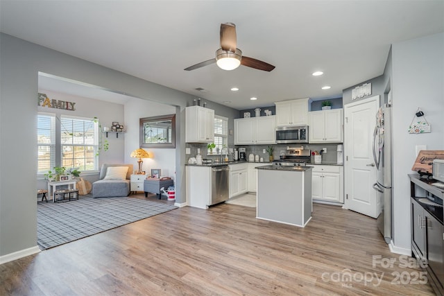 kitchen featuring appliances with stainless steel finishes, light wood-style floors, open floor plan, white cabinets, and a kitchen island