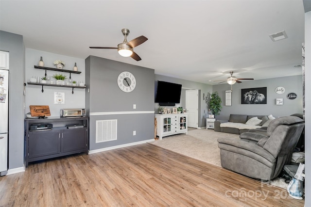 living room with light wood-style floors, visible vents, ceiling fan, and baseboards