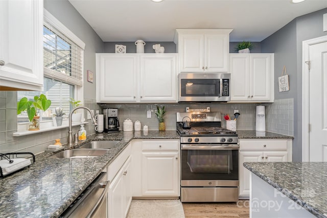 kitchen featuring light wood finished floors, stainless steel appliances, backsplash, white cabinetry, and a sink