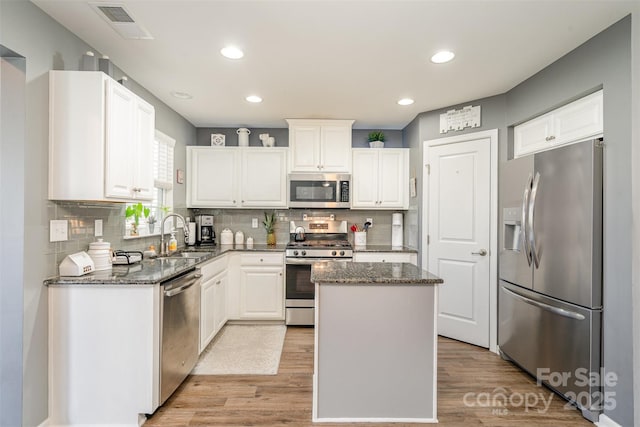 kitchen with dark stone counters, stainless steel appliances, a sink, and visible vents