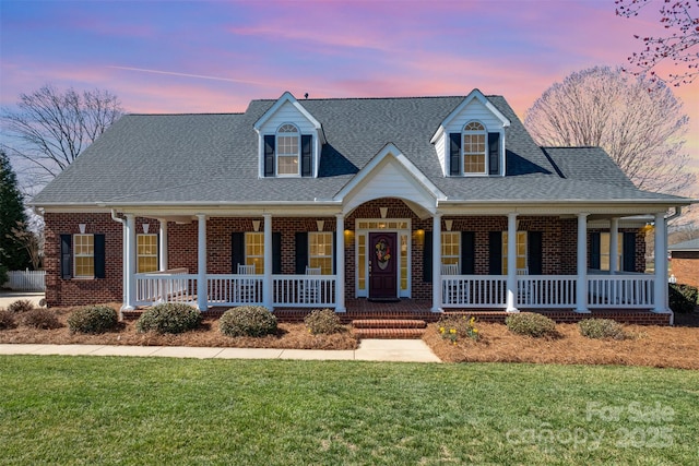 view of front of house featuring roof with shingles, a porch, a lawn, and brick siding