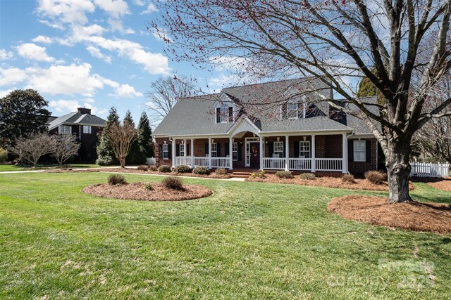 cape cod-style house with covered porch, a front yard, fence, and brick siding