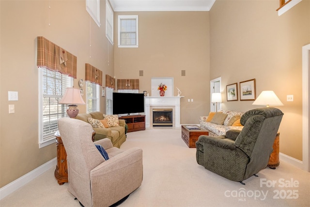 living room with carpet floors, a glass covered fireplace, ornamental molding, and baseboards