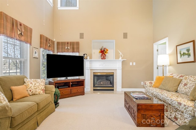 living room featuring carpet floors, a towering ceiling, and a glass covered fireplace