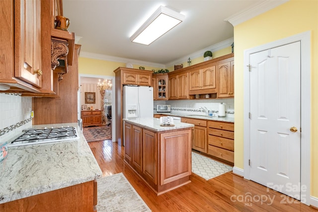 kitchen featuring light wood-style flooring, white appliances, a kitchen island, ornamental molding, and brown cabinetry