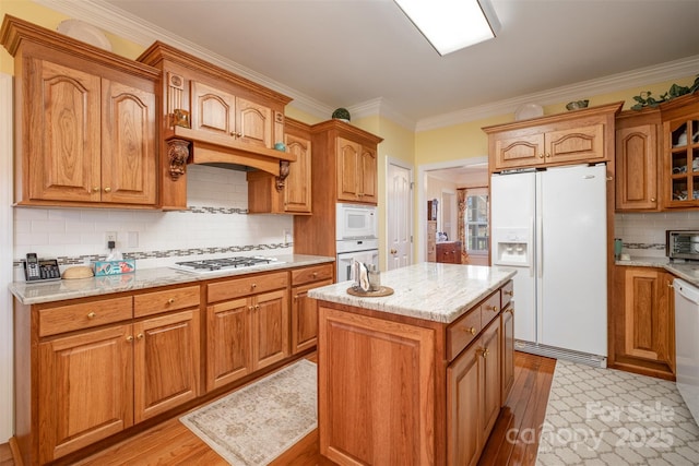 kitchen with white appliances, light wood-type flooring, backsplash, light stone countertops, and crown molding