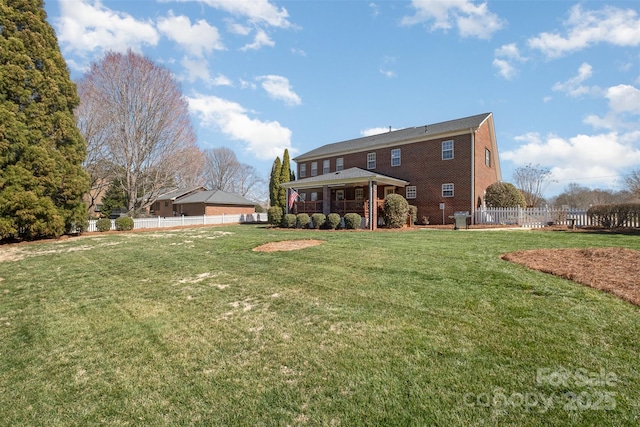 back of house featuring brick siding, a lawn, and fence