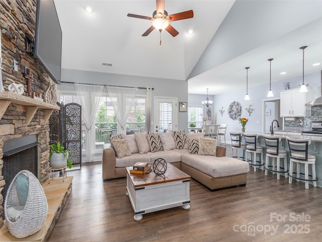 living room with dark hardwood / wood-style flooring, ceiling fan with notable chandelier, a fireplace, and high vaulted ceiling