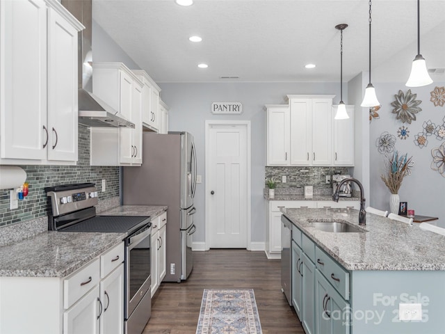kitchen featuring sink, wall chimney range hood, white cabinetry, stainless steel appliances, and decorative light fixtures