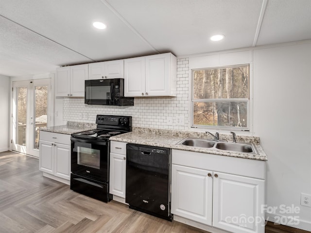 kitchen with sink, black appliances, white cabinets, light parquet floors, and backsplash