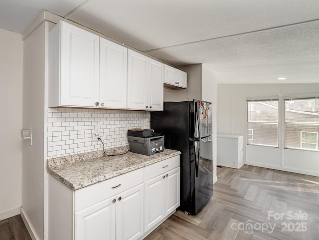 kitchen with light parquet floors, white cabinetry, backsplash, light stone countertops, and black fridge