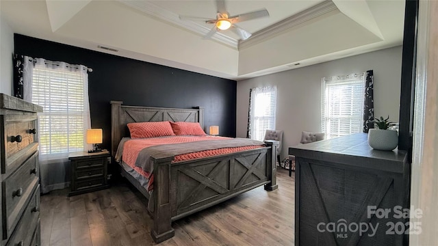 bedroom featuring hardwood / wood-style flooring, crown molding, multiple windows, and a tray ceiling