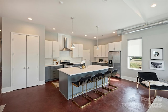 kitchen featuring appliances with stainless steel finishes, decorative light fixtures, an island with sink, white cabinets, and wall chimney exhaust hood