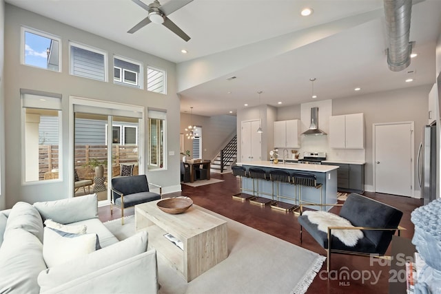 living room featuring ceiling fan with notable chandelier, dark hardwood / wood-style floors, sink, and a high ceiling