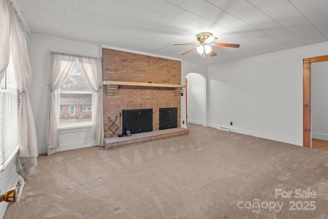 unfurnished living room with crown molding, ceiling fan, a brick fireplace, and light carpet