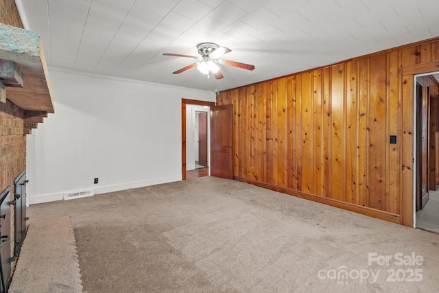 unfurnished living room with ornamental molding, carpet floors, wooden walls, and a fireplace