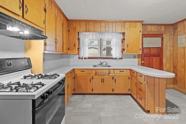 kitchen featuring white range with gas cooktop, kitchen peninsula, sink, and wood walls