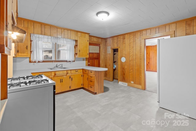 kitchen featuring range with gas stovetop, wooden walls, sink, white fridge, and crown molding