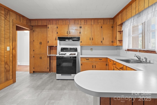 kitchen featuring sink, wooden walls, extractor fan, range with gas stovetop, and kitchen peninsula