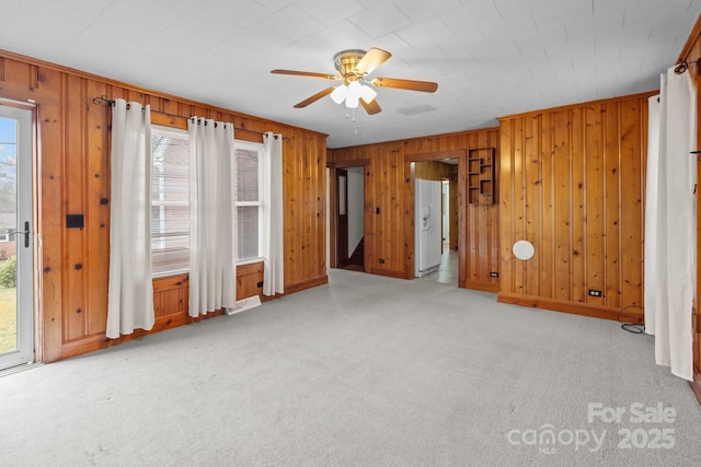 carpeted empty room featuring ceiling fan and wood walls