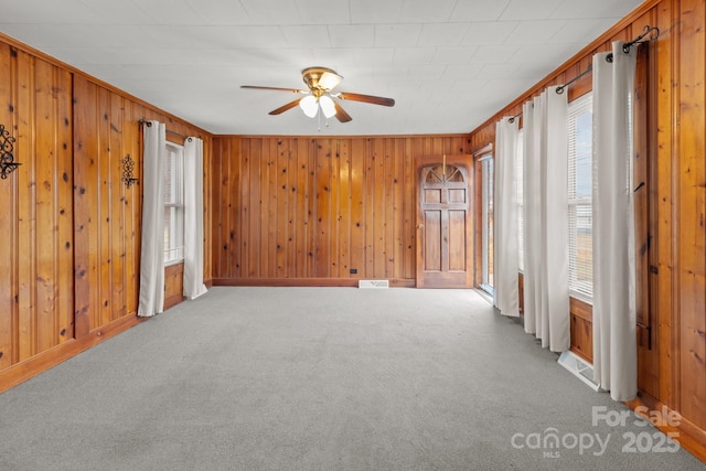 unfurnished room featuring ceiling fan, wooden walls, ornamental molding, and carpet flooring