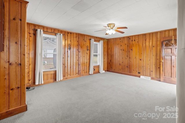 empty room featuring carpet, wooden walls, and ceiling fan