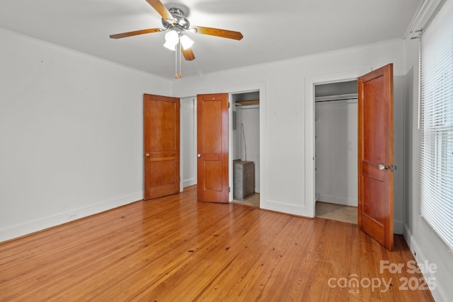 unfurnished bedroom featuring ceiling fan, light hardwood / wood-style floors, and multiple closets