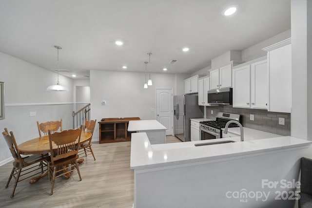 kitchen with white cabinets, hanging light fixtures, a center island, kitchen peninsula, and stainless steel appliances