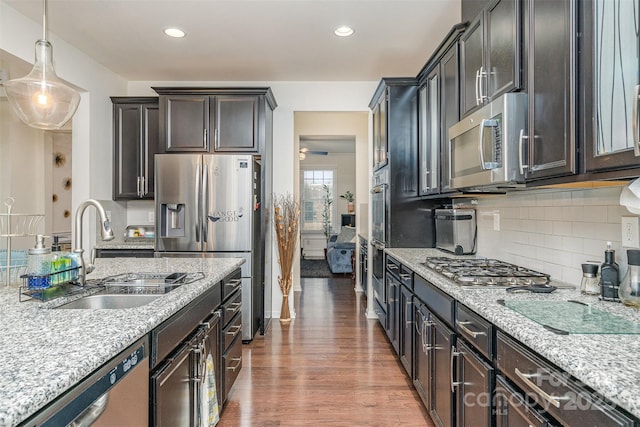 kitchen with sink, wood-type flooring, appliances with stainless steel finishes, pendant lighting, and light stone countertops