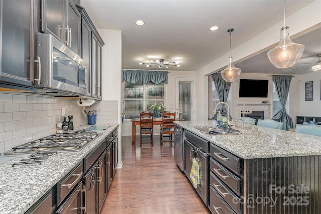 kitchen with sink, hanging light fixtures, a center island with sink, appliances with stainless steel finishes, and light stone countertops