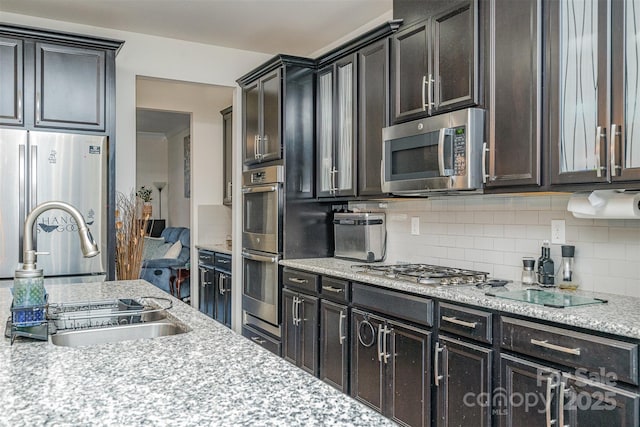 kitchen with sink, appliances with stainless steel finishes, tasteful backsplash, light stone counters, and dark brown cabinetry