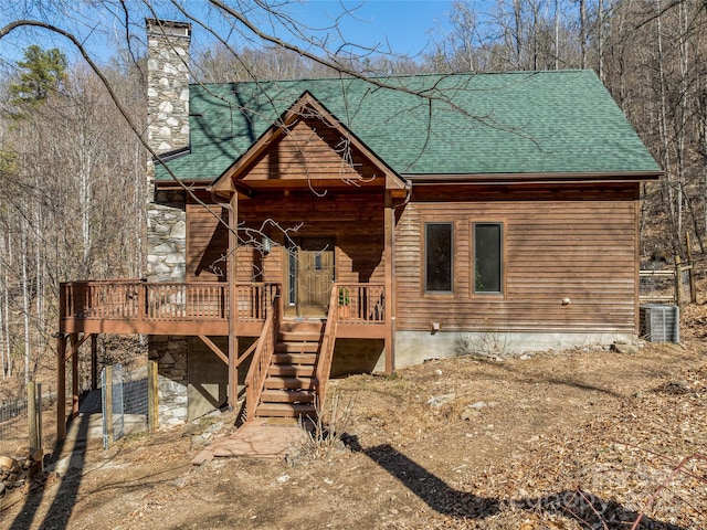 view of front of home featuring a deck, central air condition unit, a shingled roof, stairs, and a chimney