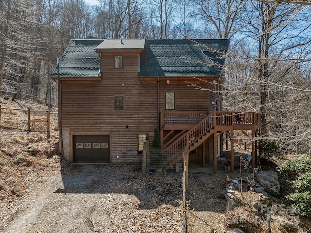 back of house with dirt driveway, roof with shingles, stairway, and an attached garage