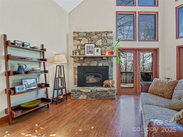 living area with a fireplace, high vaulted ceiling, wood finished floors, and french doors